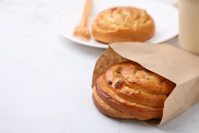Delicious roll with raisins in paper bag on white table, closeup and space for text. Sweet bun