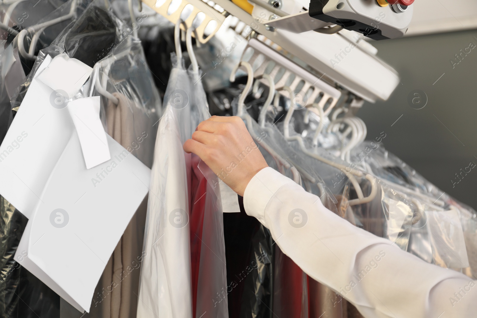 Photo of Female worker taking clothes from garment conveyor at dry-cleaner's, closeup