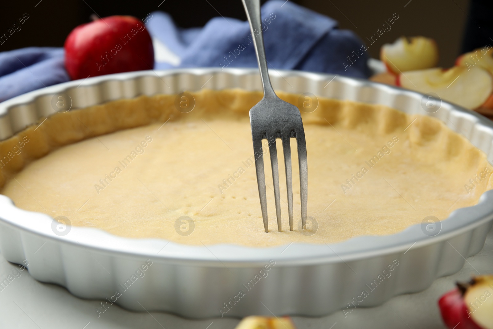 Photo of Making holes in raw dough for traditional English apple pie with fork on white table, closeup