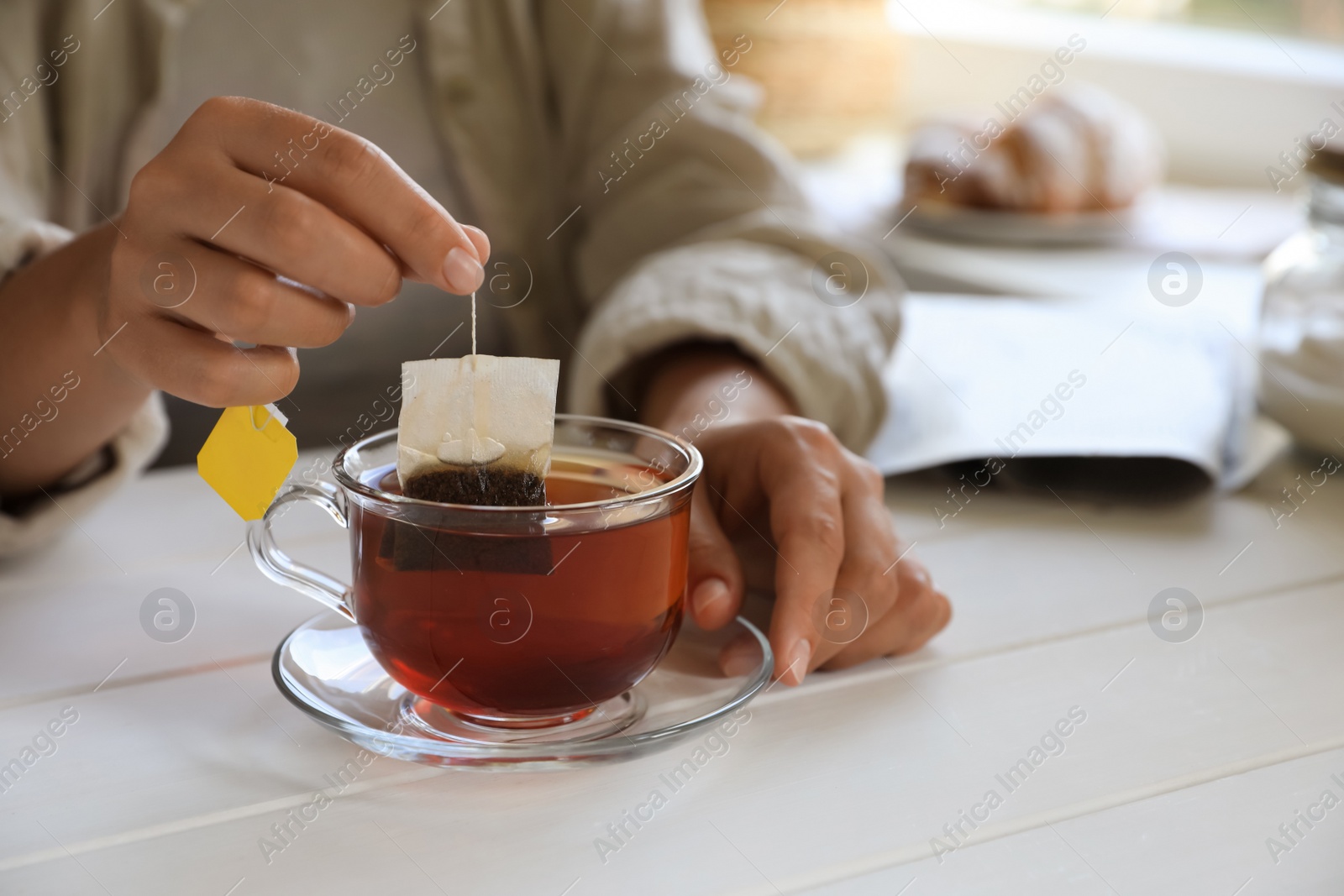 Photo of Woman taking tea bag out of cup at white wooden table indoors, closeup. Space for text