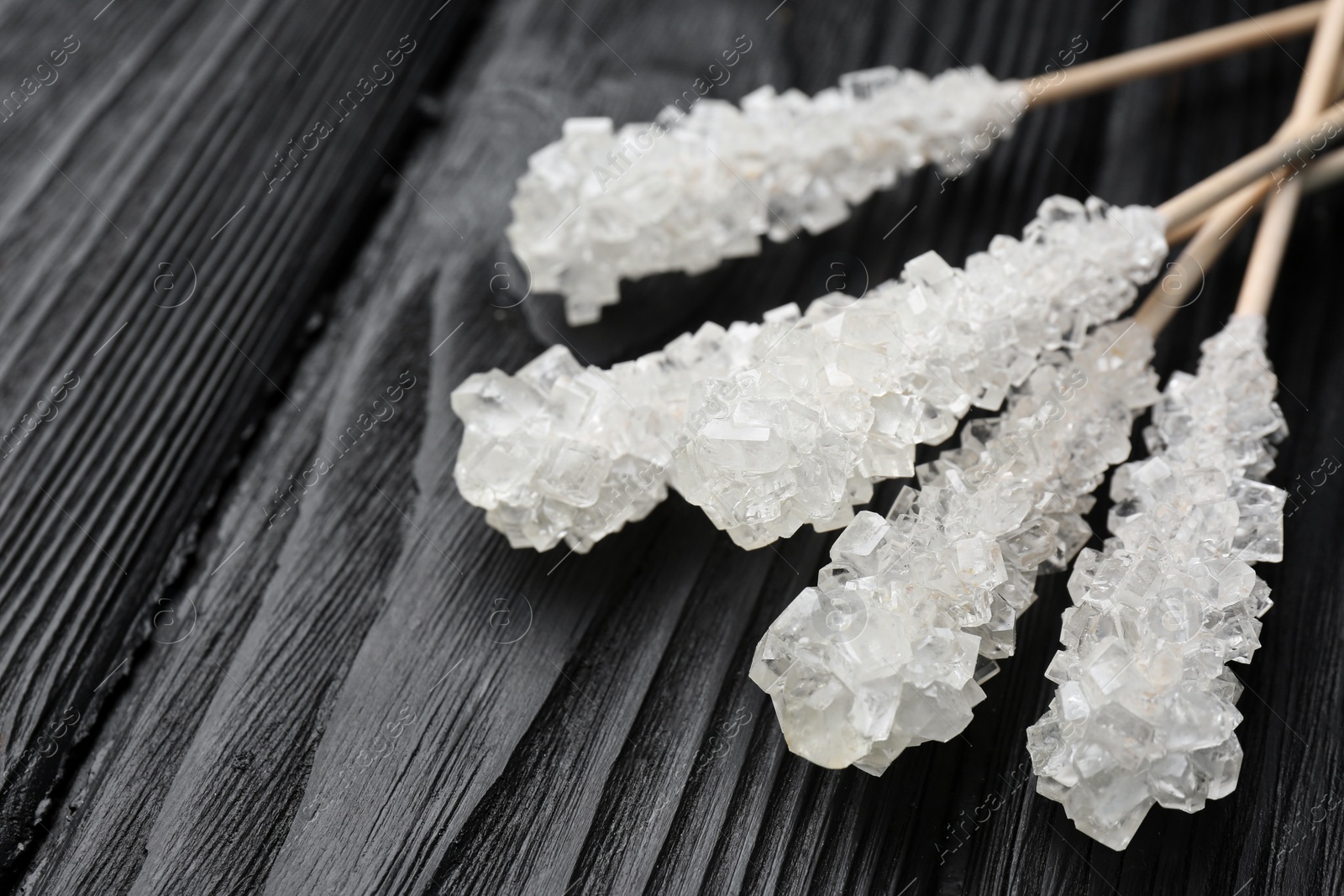 Photo of Sticks with sugar crystals on black wooden table, closeup. Tasty rock candies