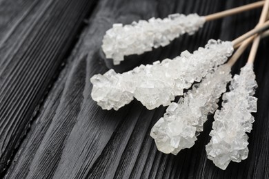 Photo of Sticks with sugar crystals on black wooden table, closeup. Tasty rock candies