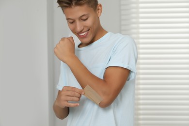 Photo of Handsome man putting sticking plaster onto elbow indoors