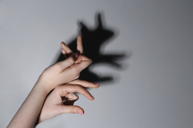 Photo of Shadow puppet. Woman making hand gesture like rabbit on grey background, closeup. Space for text