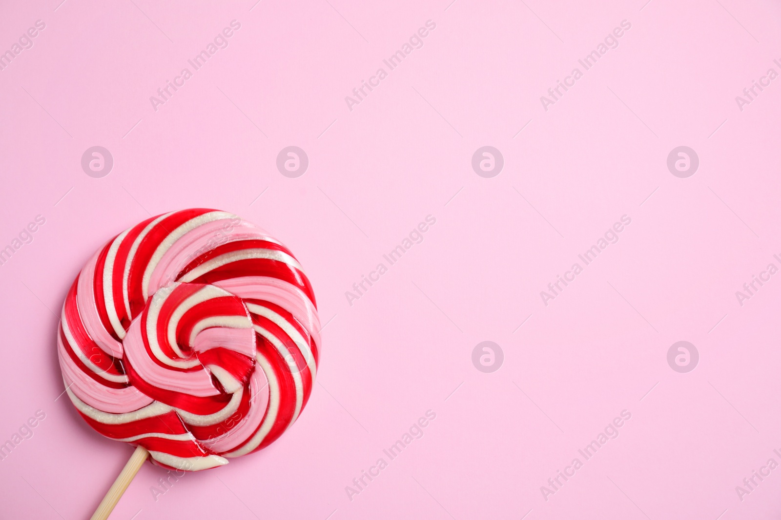 Photo of Stick with colorful lollipop swirl on pink background, top view. Space for text