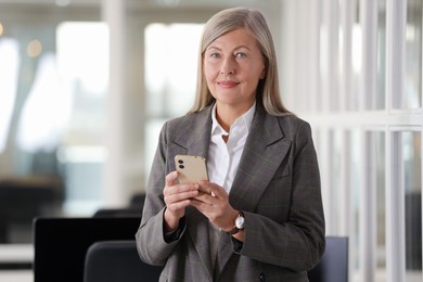 Photo of Confident woman with smartphone in office. Lawyer, businesswoman, accountant or manager