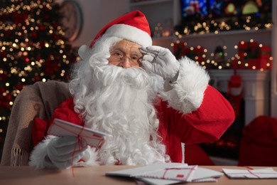 Santa Claus holding letter at table in room decorated for Christmas