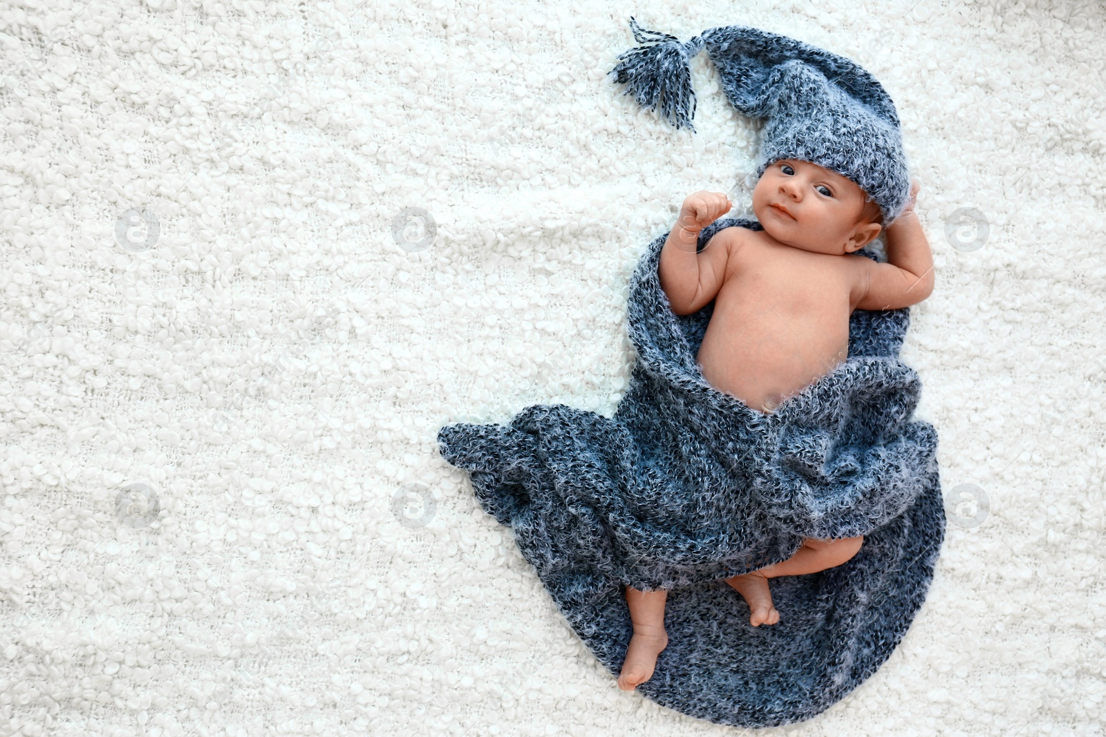 Photo of Cute little baby in grey hat and plaid lying on soft blanket, top view. Space for text