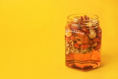 Different nuts and honey in jar on yellow background. Space for text