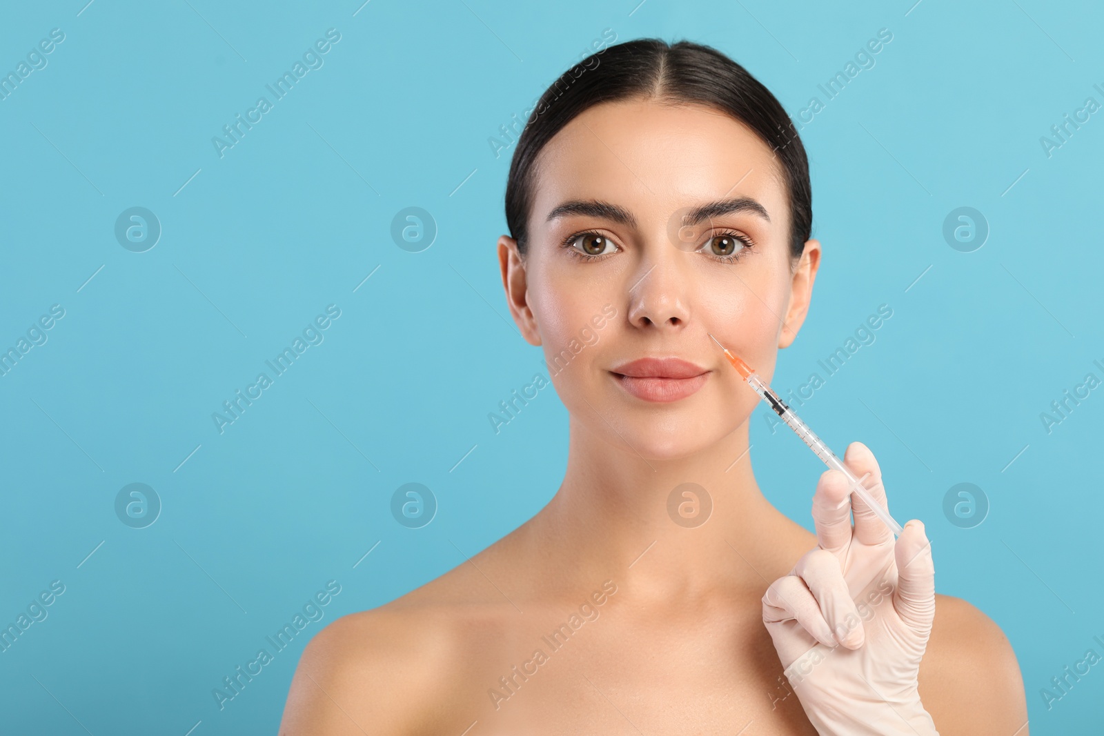 Photo of Doctor giving facial injection to young woman on light blue background, space for text. Cosmetic surgery