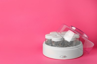 Modern yogurt maker with empty jars on pink background, space for text