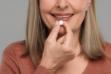 Photo of Senior woman taking pill on grey background, closeup