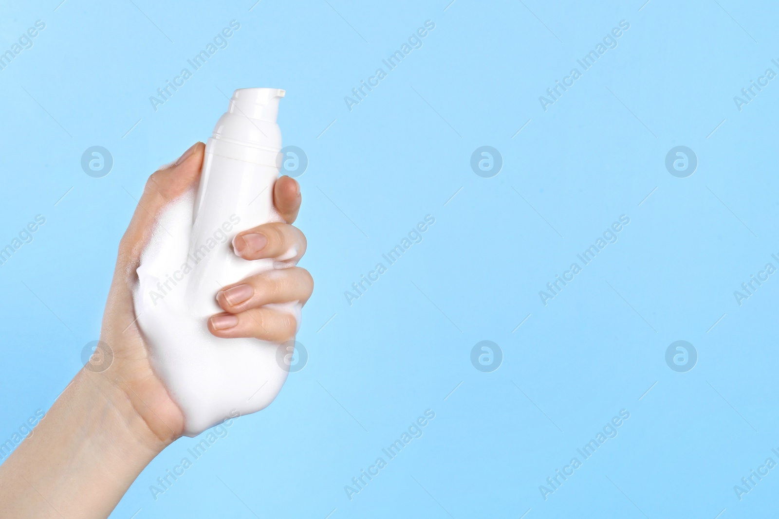 Photo of Woman with bottle of care product and cleansing foam on light blue background, closeup. Space for text