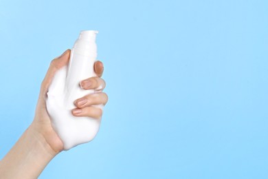 Woman with bottle of care product and cleansing foam on light blue background, closeup. Space for text