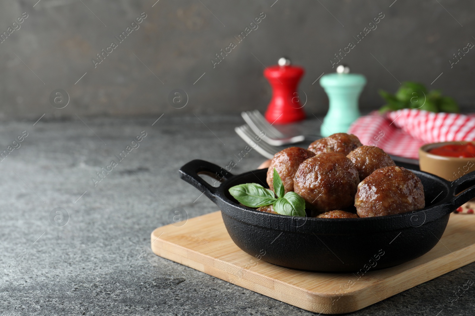 Photo of Tasty cooked meatballs with basil served on grey table. Space for text