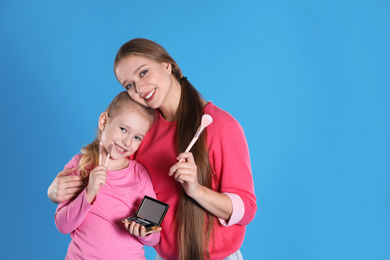 Photo of Happy mother and daughter with cosmetic on blue background. Space for text