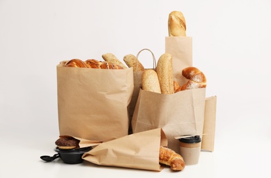 Different fresh bakery products in paper bags on white background