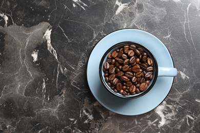 Cup with roasted coffee beans and space for text on grey background, top view