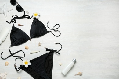 Flat lay composition with black swimsuit and beach accessories on light stone background. Space for text