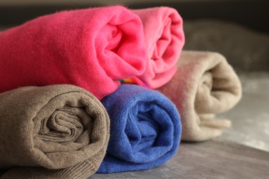 Photo of Rolled color sweaters on gray table, closeup