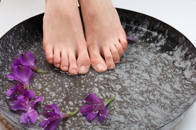 Woman soaking her feet in bowl with water and flowers, closeup. Spa treatment