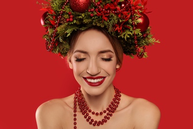 Beautiful young woman wearing Christmas wreath on red background