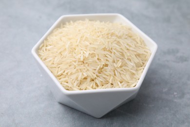 Raw rice in bowl on light grey table, closeup