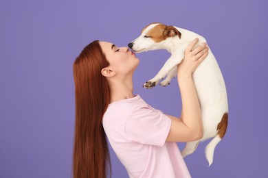 Woman kissing cute Jack Russell Terrier dog on violet background