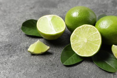 Photo of Fresh ripe limes and leaves on grey table, closeup