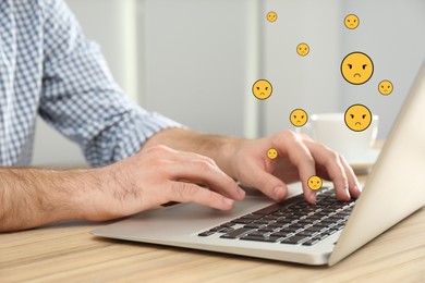 Social media dislike reaction. Man using laptop at table, closeup. Angry face emoji illustrations over device