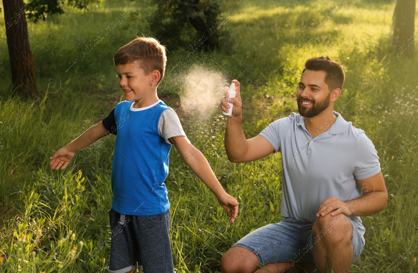 Photo of Man applying insect repellent on his son in park. Tick bites prevention
