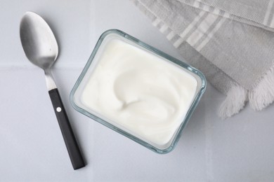 Photo of Delicious natural yogurt in glass bowl and spoon on white tiled table, top view