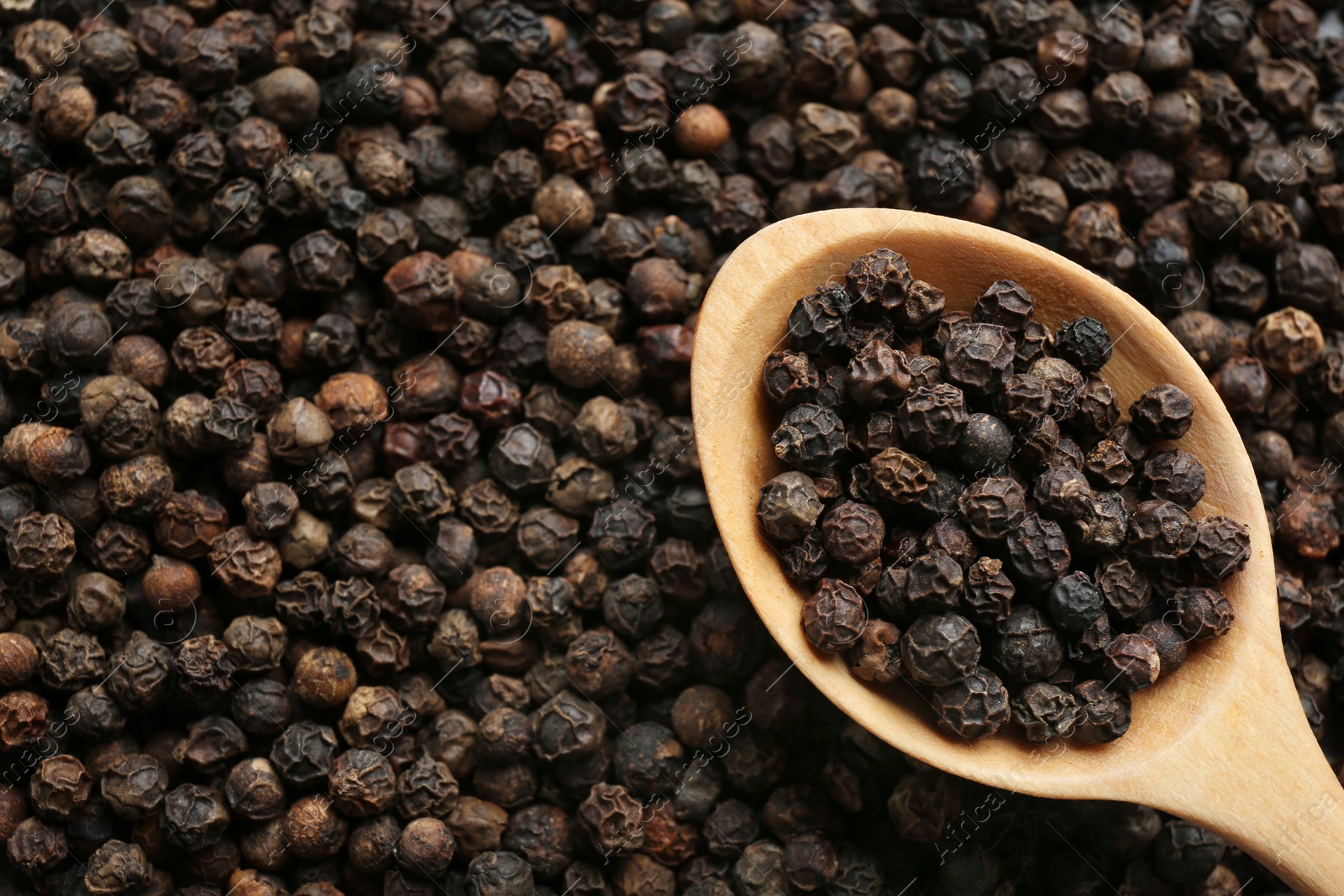 Photo of Closeup of wooden spoon with black peppercorns, top view
