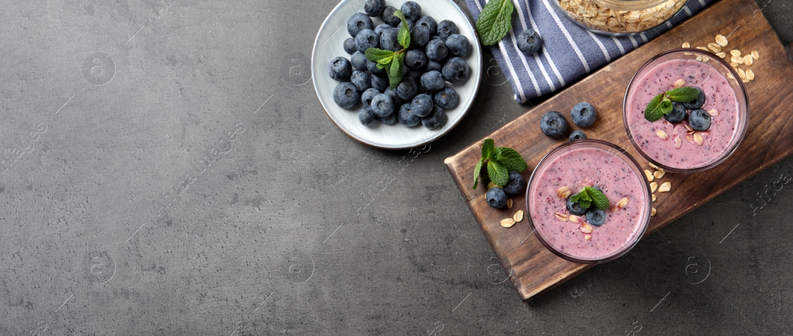 Image of Glasses of tasty blueberry smoothie with oatmeal on dark grey table, flat lay with space for text. Banner design