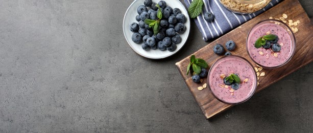 Image of Glasses of tasty blueberry smoothie with oatmeal on dark grey table, flat lay with space for text. Banner design