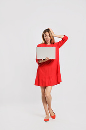 Full length portrait of emotional woman with modern laptop on light grey background