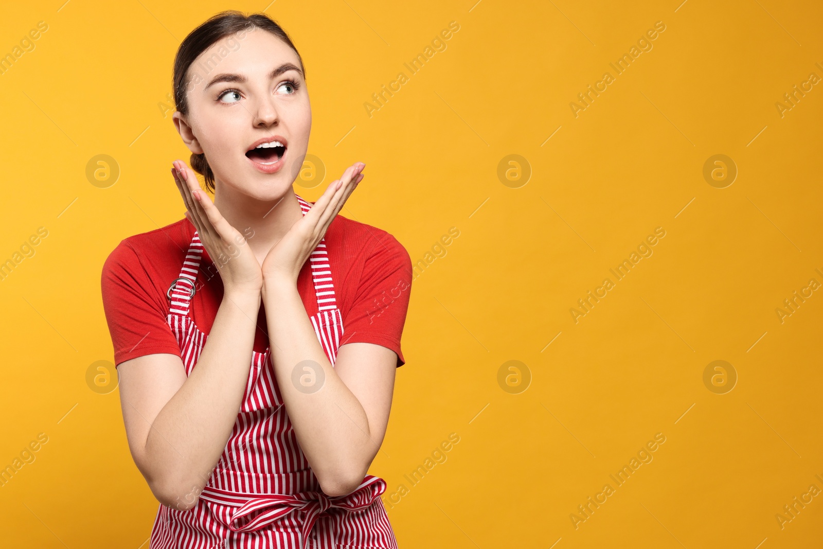 Photo of Beautiful young woman in clean striped apron on orange background. Space for text