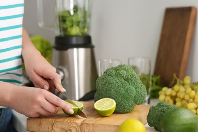 Photo of Woman cutting lime for smoothie in kitchen, closeup