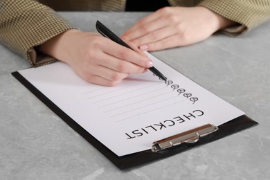 Photo of Woman filling Checklist at grey marble table, closeup