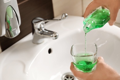 Photo of Man pouring mouthwash from bottle into glass in bathroom, closeup. Teeth care