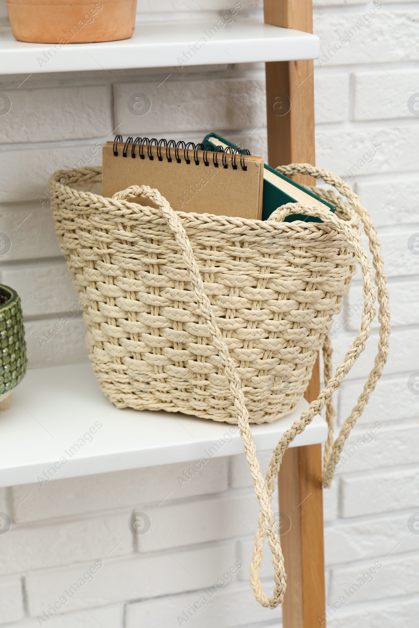 Photo of Stylish beach bag with notebooks on shelf indoors