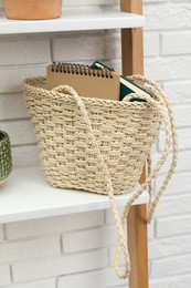 Stylish beach bag with notebooks on shelf indoors