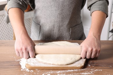 Man rolling dough at table in kitchen, closeup