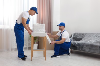 Photo of Workers wrapping chair in stretch film indoors