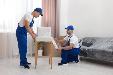 Workers wrapping chair in stretch film indoors