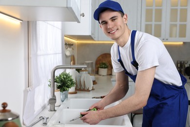 Photo of Smiling plumber repairing sink with screwdriver in kitchen