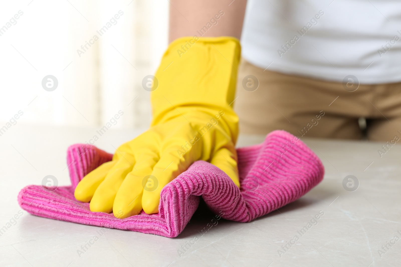 Photo of Woman in gloves wiping grey table with rag indoors, closeup