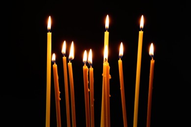 Many burning church candles on dark background
