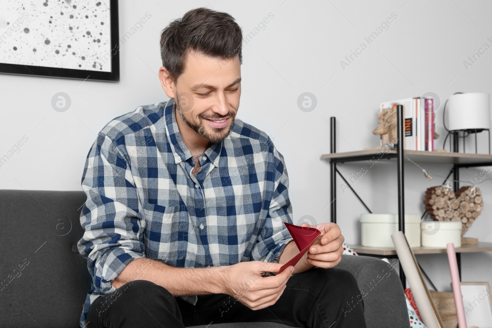 Photo of Happy man holding greeting card on sofa in living room