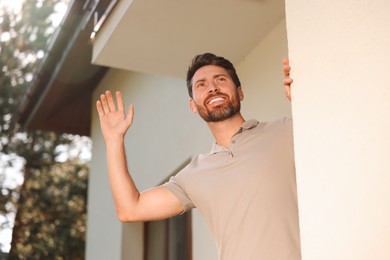 Photo of Neighbor greeting. Happy man waving near house outdoors, low angle view